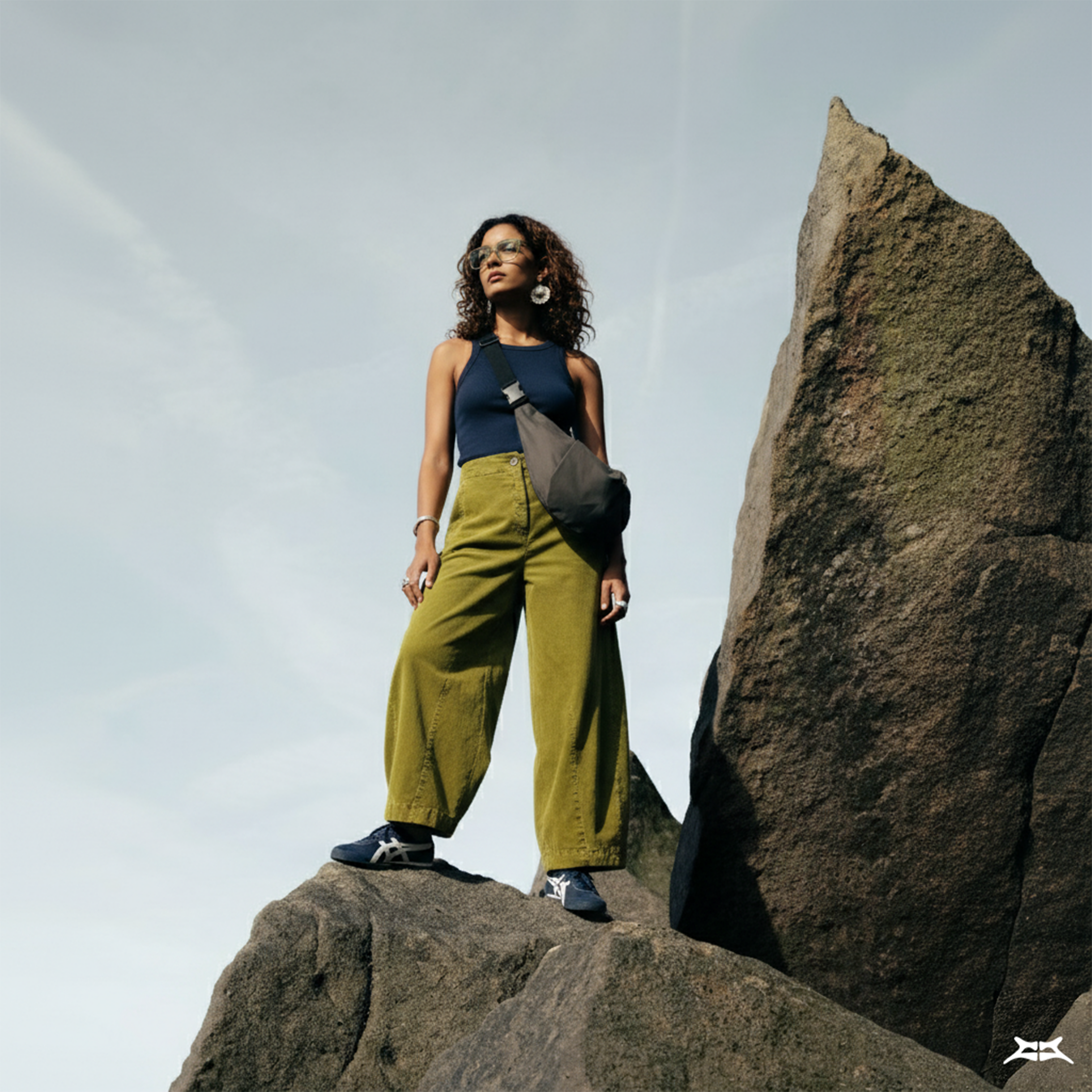 Woman standing on a rock, wearing a grey crescent crossbody sling bag.