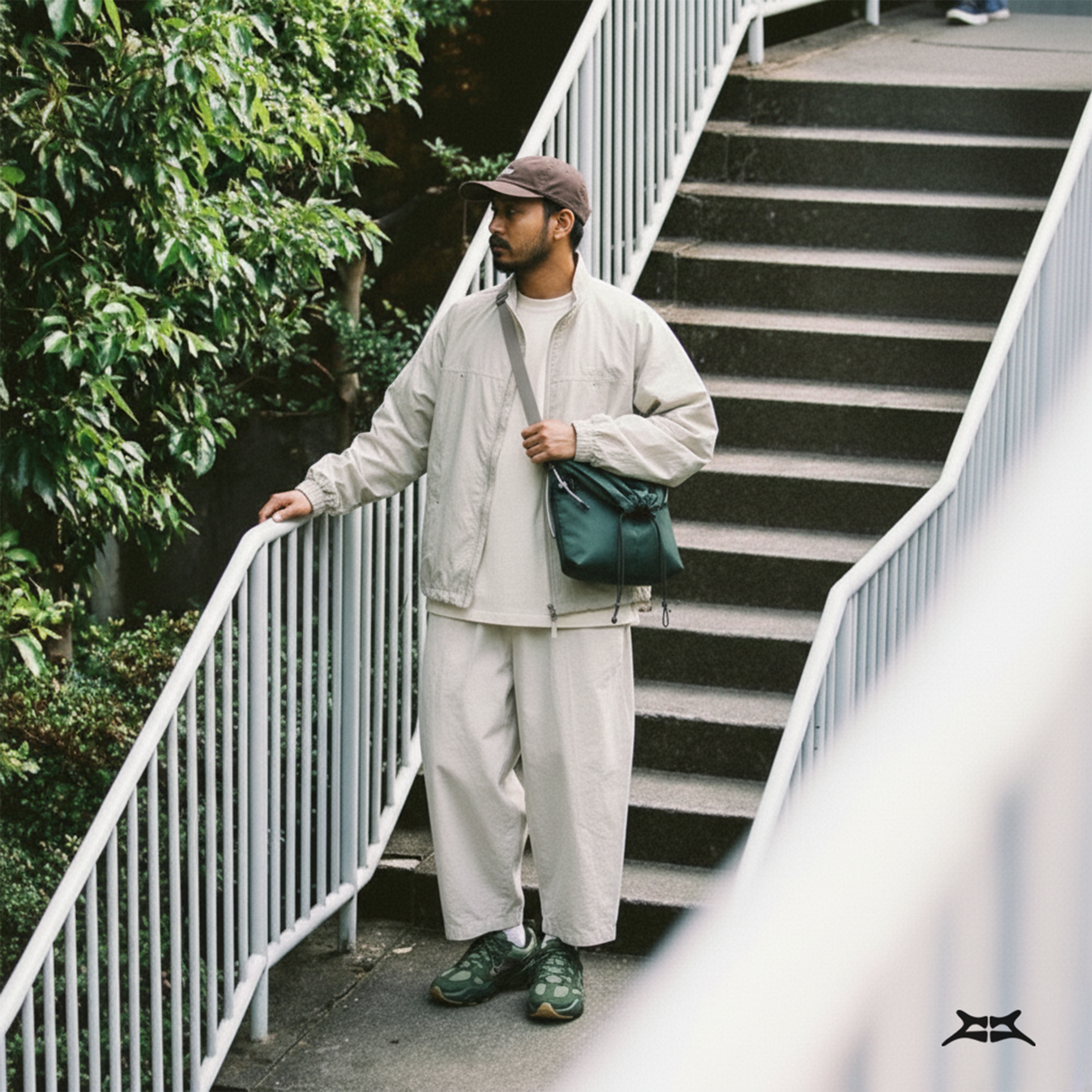 Man in a casual outfit, wearing a forest green water-resistant sling bag on stairs.
