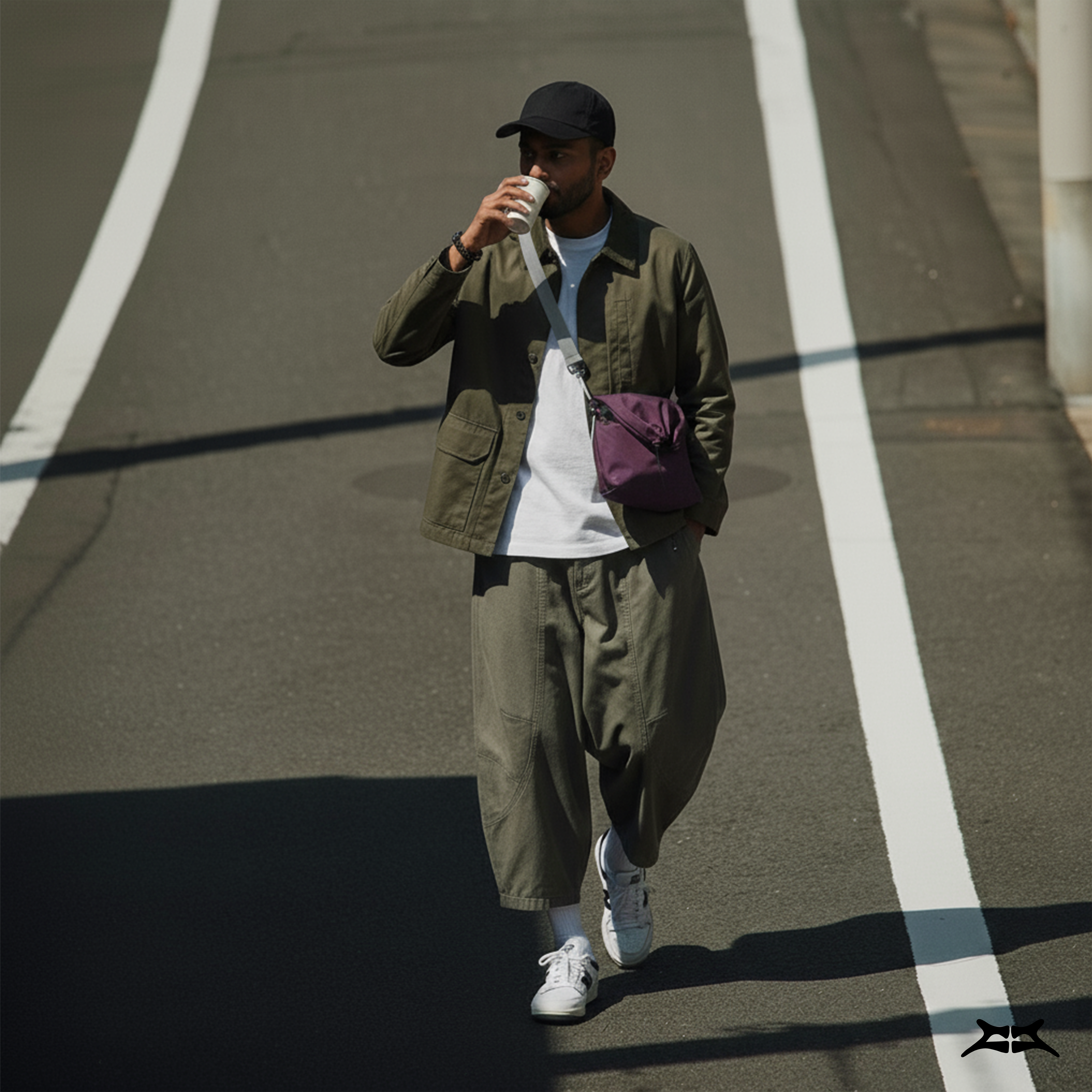 Man in street style fashion, walking and carrying a maroon crossbody sling bag.